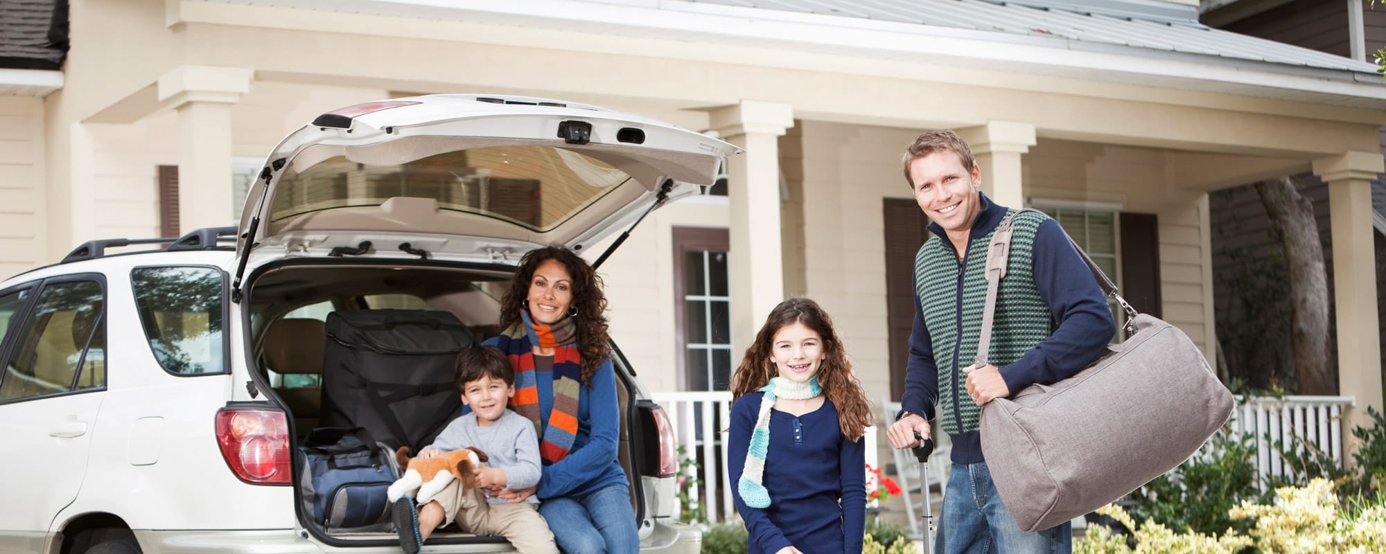 Image of family standing in front of their car while parked in driveway of their home